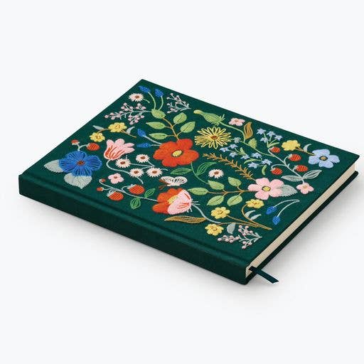 The Strawberry Fields Embroidered Sketchbook is a dark green hardcover journal with vibrant floral embroidery and a black ribbon bookmark.