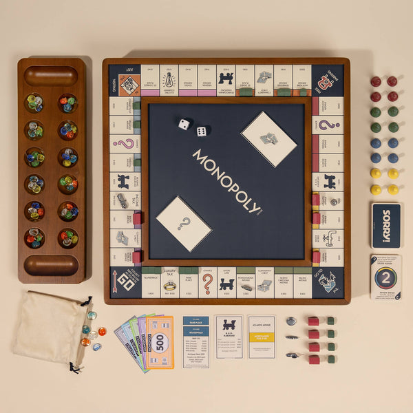 The 3-in-1 Game Collection: Monopoly, Sorry & Mancala is arranged on a beige surface, with game pieces, cards, dice, money, and a reversible board showing the Monopoly logo for family fun.