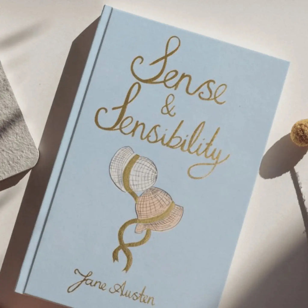 The Sense and Sensibility | Collector's Edition | Hardcover Book features a light blue cover with gold cursive text and two vintage hats with ribbons illustrated on the front.