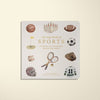 The "Newborn Gift Set" features a Maileg Teddy in a sporty organic cotton romper and a handmade wooden rattle, all nestled among vibrant illustrations of sports equipment on the cover of the children's book "Our Big Book of Sports.