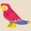 The Holztiger Parrot, a colorful handcrafted wooden figurine with a pink body, yellow beak and feet, white accents, and blue tail, is shown in profile on a beige background. Ships in one week as part of the HOLZTIGER collection.