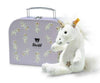 The Steiff Unica Dangling Plush Toy Unicorn, featuring a gold star on its leg, sits in front of a light purple suitcase adorned with unicorn illustrations and a bear logo, promising magical adventures.