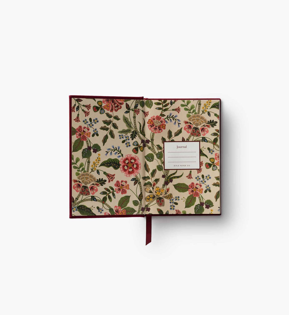 The Gracie Mini Embroidered Journal is an open hardcover with floral and butterfly inner covers, blank unlined pages, a labeled "Journal" insert on the right, and a red ribbon bookmark hanging from the center.
