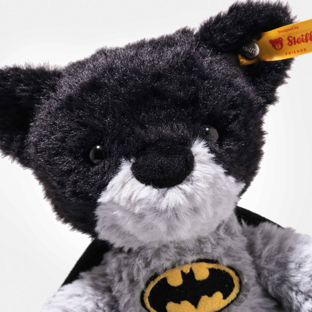 The Steiff Batman Teddy Bear, 12 Inches, features black and gray fur, a cape, and a yellow Batman logo on its chest. A signature yellow Steiff tag is attached to its ear—ideal for Dark Knight and DC Universe fans.