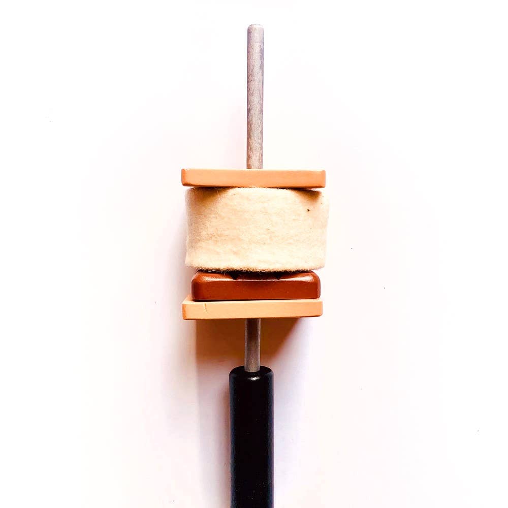 The Wooden Camp Fire Set features a vertical metal rod holding a cylindrical felt piece between two rectangular wooden blocks, topped with a black handle—ideal for indoor camping or kids' pretend play, shown on a white background.