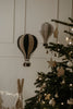Two decorative Hot Air Balloon - Black ornaments hang on a white wall beside a Christmas tree with lights and ornaments, creating a cozy, festive atmosphere with warm lighting—perfect for decorating children's rooms.