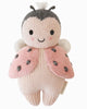 The Cuddle + Kind Baby Ladybug is a hand-knit plush toy made from natural Peruvian cotton yarn, featuring pink wings, black spots, and blushing cheeks. Crafted using fair trade practices for a soft and adorable look.