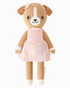 Cuddle + Kind Bea The Dog is a hand-knit stuffed doll with a beige body, white accents, and a smiling face. She wears a pink dress with pastel stripes and a pink flower on her head, and is filled with hypoallergenic polyfill.