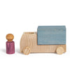 A Lubulona Wooden Truck - Grey with natural wood wheels and a blue block on its back sits beside a small purple peg figure, all from the charming Lubu Town collection, displayed on a white background.