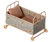 The PRE-ORDER: Cot Bed, Micro - Powder features a floral-patterned fabric in brown and beige hues, includes a matching pillow and blanket, and is set on four wooden wheels. Estimated ship date: Early October.