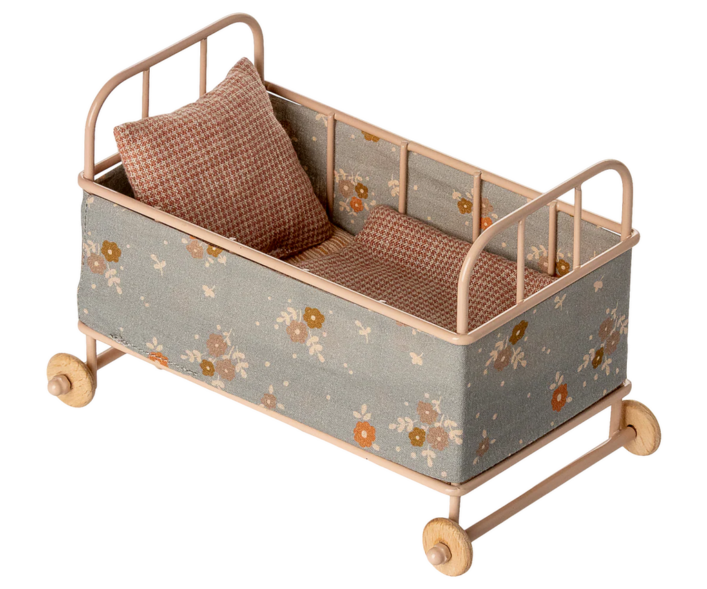 The PRE-ORDER: Cot Bed, Micro - Powder features a floral-patterned fabric in brown and beige hues, includes a matching pillow and blanket, and is set on four wooden wheels. Estimated ship date: Early October.