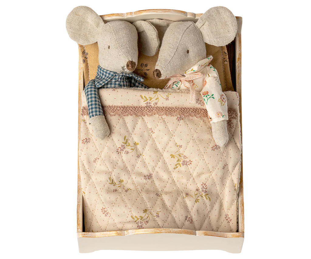 Two fabric mice, one with a blue checkered scarf and the other in a floral dress, are snug under a quilted blanket in the PRE-ORDER: Bed, Mouse - Off White (ships early October), creating a charming scene.