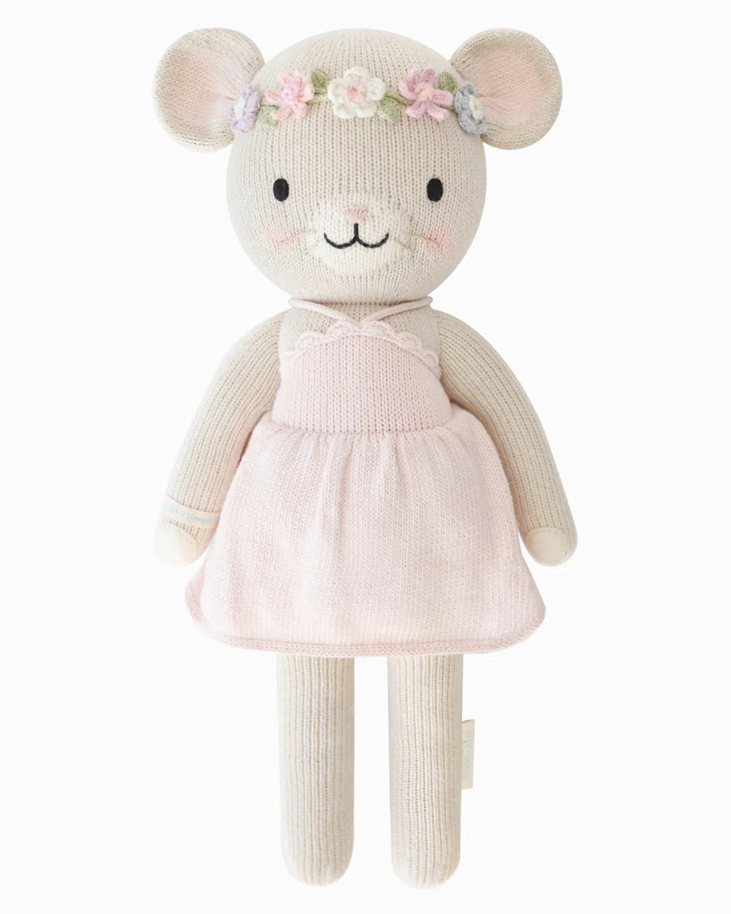 Cuddle + Kind Emma The Mouse is a soft, knitted doll handmade with hypoallergenic materials. She wears a pale pink dress and pastel flower crown, featuring embroidered facial details, pink blush on her cheeks, and rounded ears.