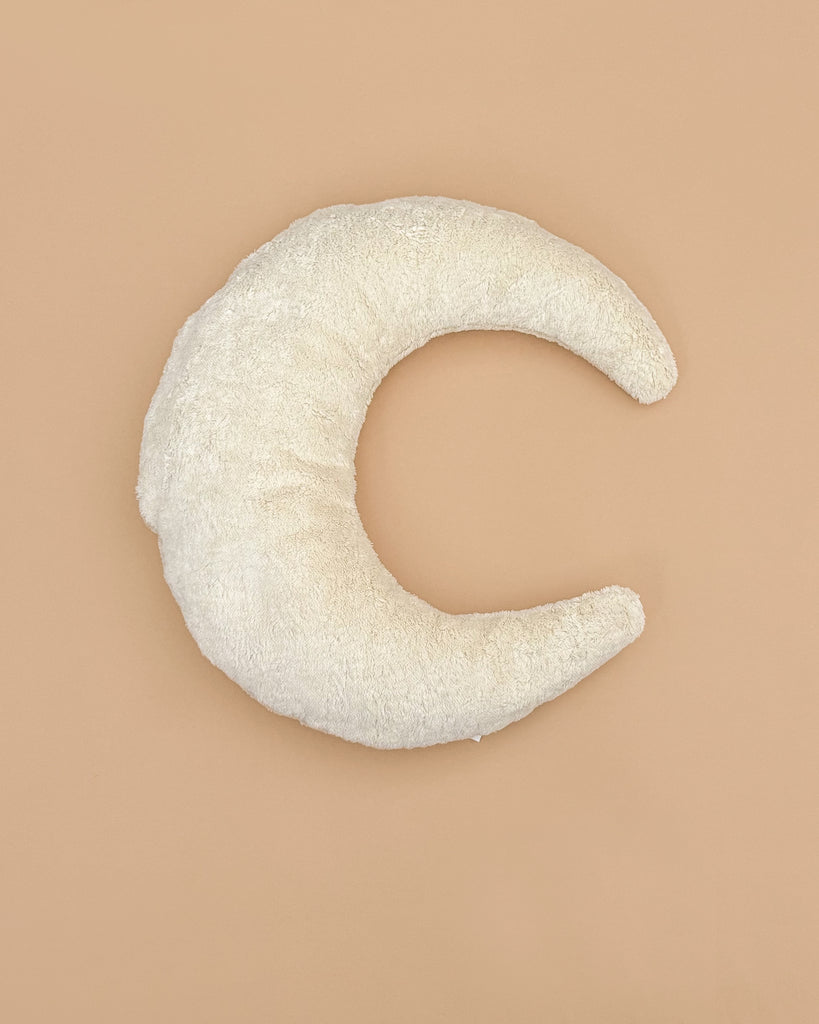 The Senger Naturwelt - Moon Nursing and Neck Pillow, crafted with GOTS-certified materials and covered in white fabric, is shaped like a soft crescent moon and placed on a plain beige background.