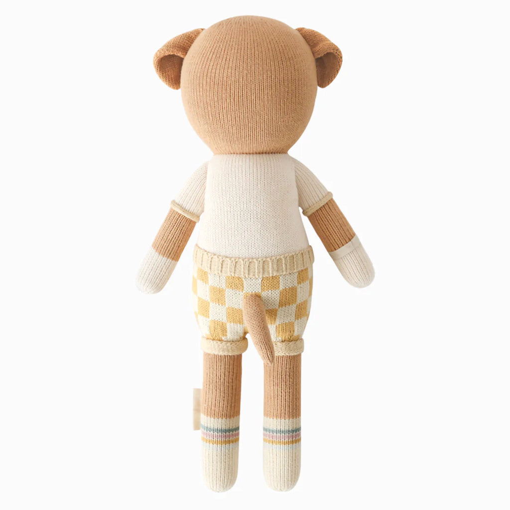 Cuddle + Kind George The Dog is a hand-knit doll, shown from the back, wearing a cream shirt and yellow checkered shorts. It features small round ears, a short tail, and is filled with hypoallergenic polyfill for safe cuddles.