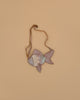 The Donsje Leather Thysa Purse - Gold Fish, a small fish-shaped bag with pastel scales and a tan adjustable strap, is displayed against a beige background.