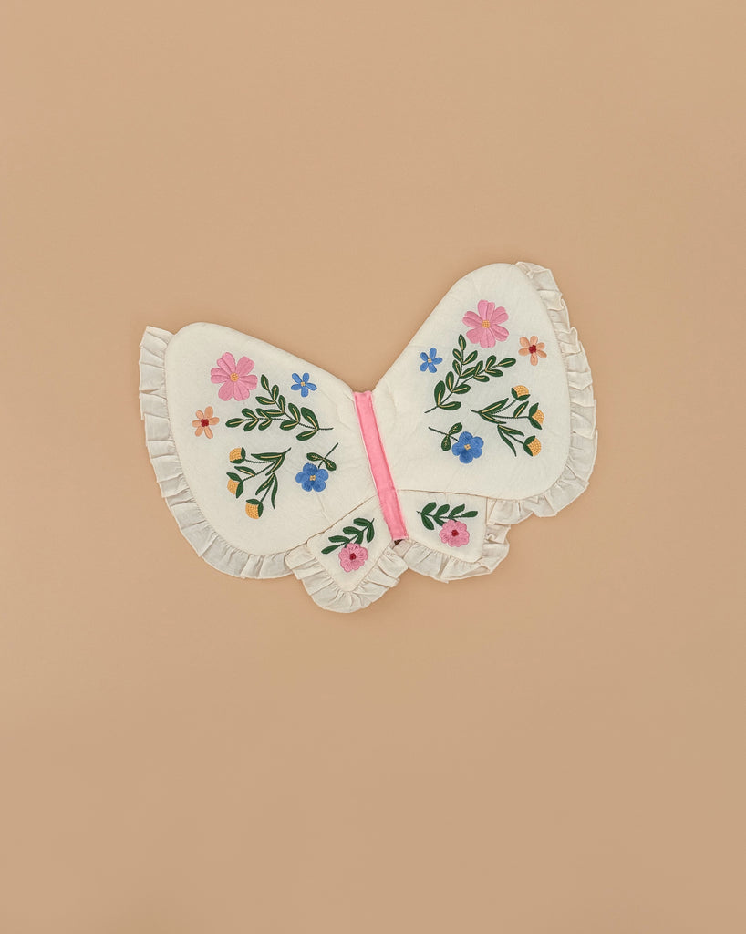 The Meri Meri Butterfly Wings feature ruffled edges and vibrant embroidered flowers on the wings, set against a plain beige background.