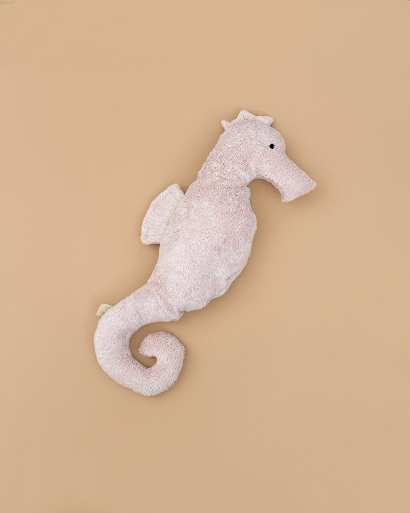 The Senger Naturwelt Cuddly Animal - Seahorse is a soft, light pink plush with a curled tail and stitched eye, resting on a beige background—GOTS-certified and perfect for little ones.