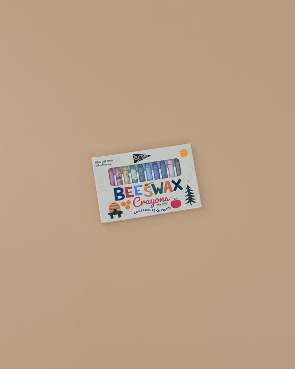 A box of 12 Beeswax Crayons – Non-Toxic with colorful sticks visible through playful, brightly illustrated packaging sits on a plain beige surface.