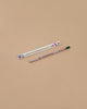 A Strawberry Plantable Pencil – Eco-Friendly with a green tip rests beside a white box adorned with red strawberries and leaves, both crafted from sustainable materials, set on a light brown background.