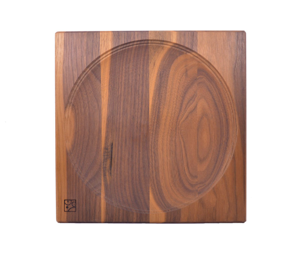 The Walnut Wood Spinning Plate is a square toy made from walnut wood, featuring a central circular groove, light and dark grain patterns, and a small logo in the bottom left corner. It is crafted to meet toy safety standards.