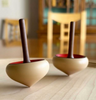 A Mader Zwirbel Spinning Top - Blue, featuring a smooth wooden base and handle, rests on a tabletop. A chair and other furniture appear blurred in the background.
