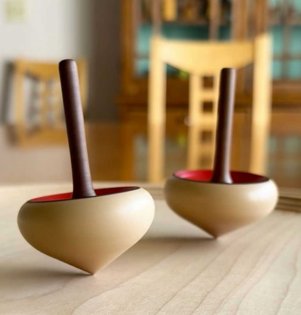 A Mader Zwirbel Spinning Top - Blue, featuring a smooth wooden base and handle, rests on a tabletop. A chair and other furniture appear blurred in the background.