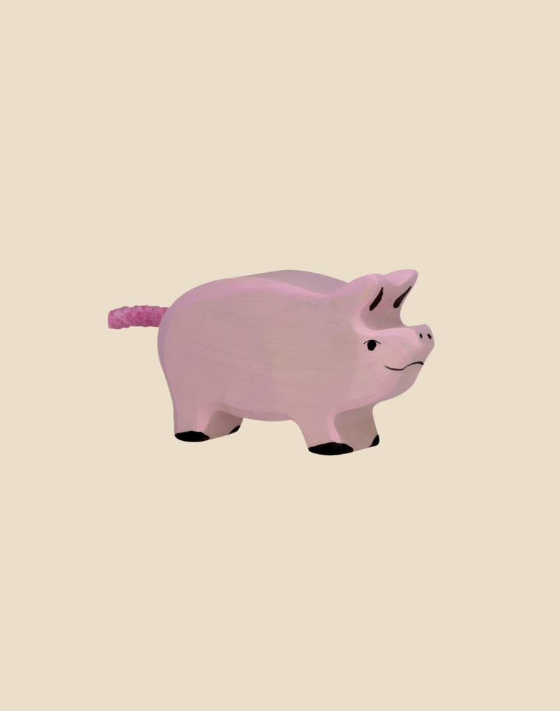 The Holztiger Piglet is a handcrafted wooden toy painted light pink with watercolors, featuring black hooves, a smiling face, and a textured pink tail. Ships in one week.