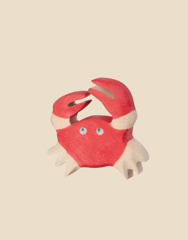 The Holztiger Crab, a red and white wooden cartoon crab with blue eyes, raises its claws against a beige background. Ships in one week.