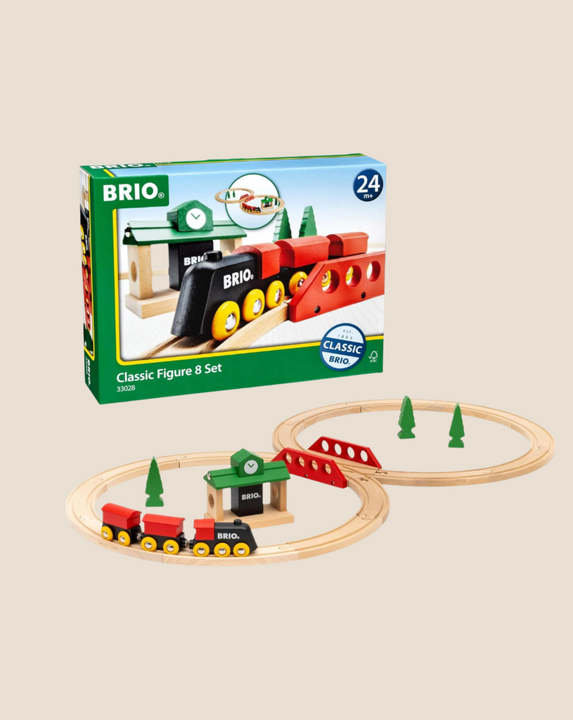 The BRIO World Train Set Classic Figure 8 Set includes an assembled figure-eight wooden track, red and yellow train cars, a green station, bridge, trees, and a sign, all displayed on a beige background.
