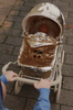 A child pushes the Konges Sloejd Sparkly Doll Pram - Golden Cherry, featuring a gold sequin cover with cherry design, while carrying a doll outdoors on a paved walkway.