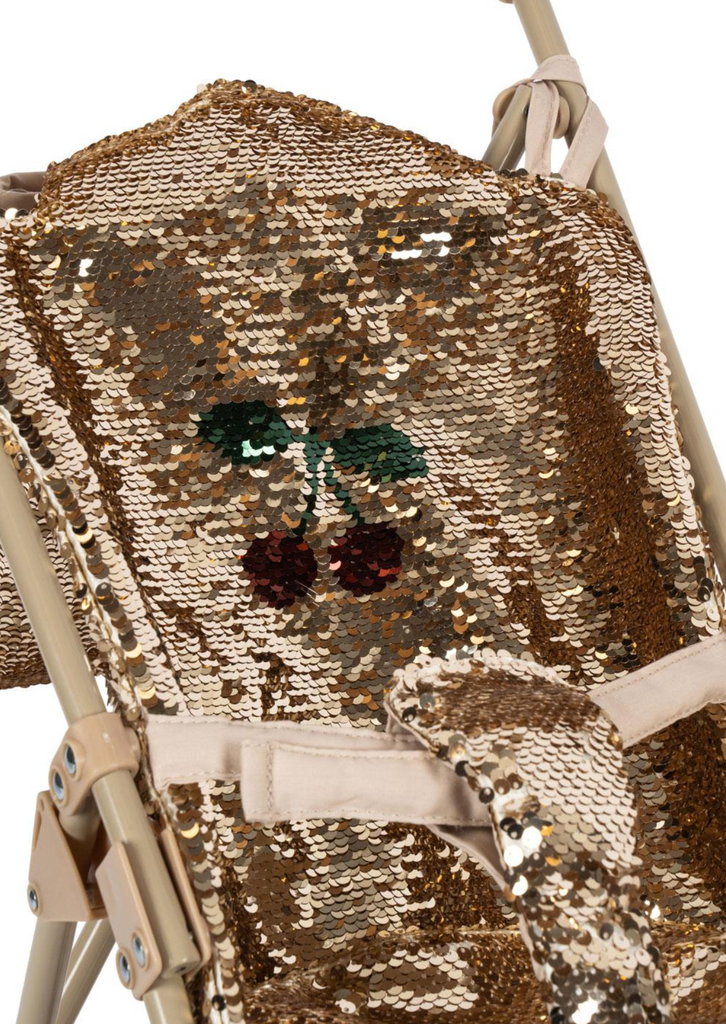 The Konges Sloejd Sparkly Sequin Doll Stroller - Golden Cherry features a beige frame and a seat covered in shiny gold sequins, adorned with an embroidered red cherry and green leaf design.