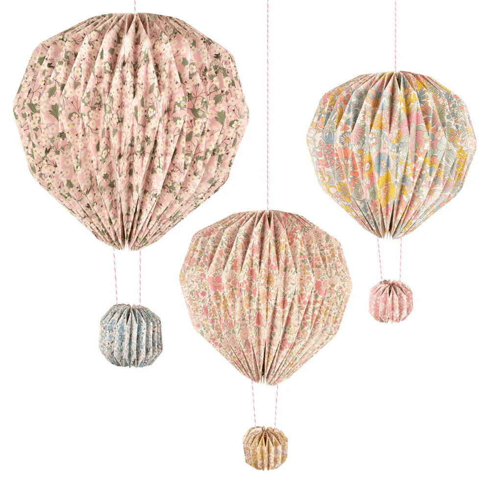 The Meri Meri x Liberty Origami Balloon Decorations feature three floral hot air balloon-shaped paper lanterns in pink, blue, and yellow, each hanging from a string with a matching small round balloon beneath.