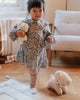 A young girl in a floral dress and pink leggings walks indoors holding a white teddy bear, while a Miffy Snuffy Stuffed Animal rests on the wooden floor in the cozy, softly lit living room.