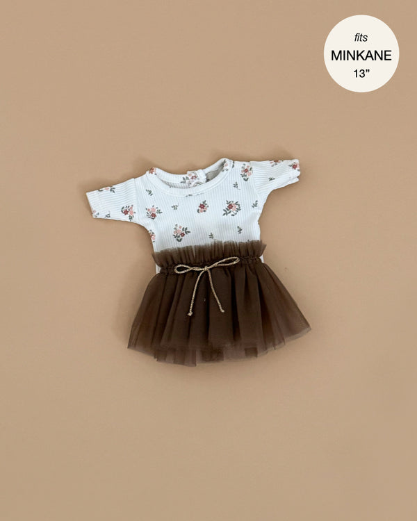 The Minikane Doll Clothing Josepha Set features a pink flower bodysuit and brown tutu, fits 13-inch Minikane dolls, is hand washable, and is shown on a beige background.