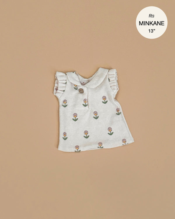 The Minikane Doll Clothing | Emile & Ida, Emilia Dress in Soft Terrycloth - Flower is a small sleeveless white dress with ruffled shoulders and brown button, designed in France for Minikane 13" and 14" dolls. Features tiny tulip flowers.