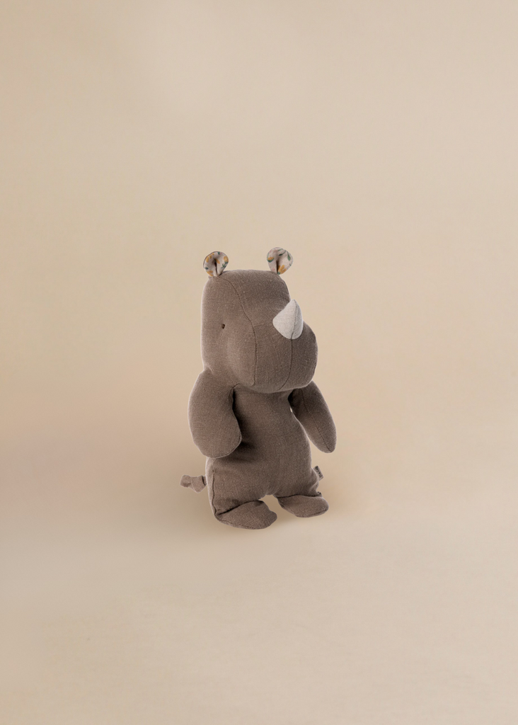 The Maileg Small Rhino - Chocolate, part of the Safari Friends collection, is a brown plush toy with a small horn, round patterned ears, soft fabric, and stitched features, shown standing on a light beige background.