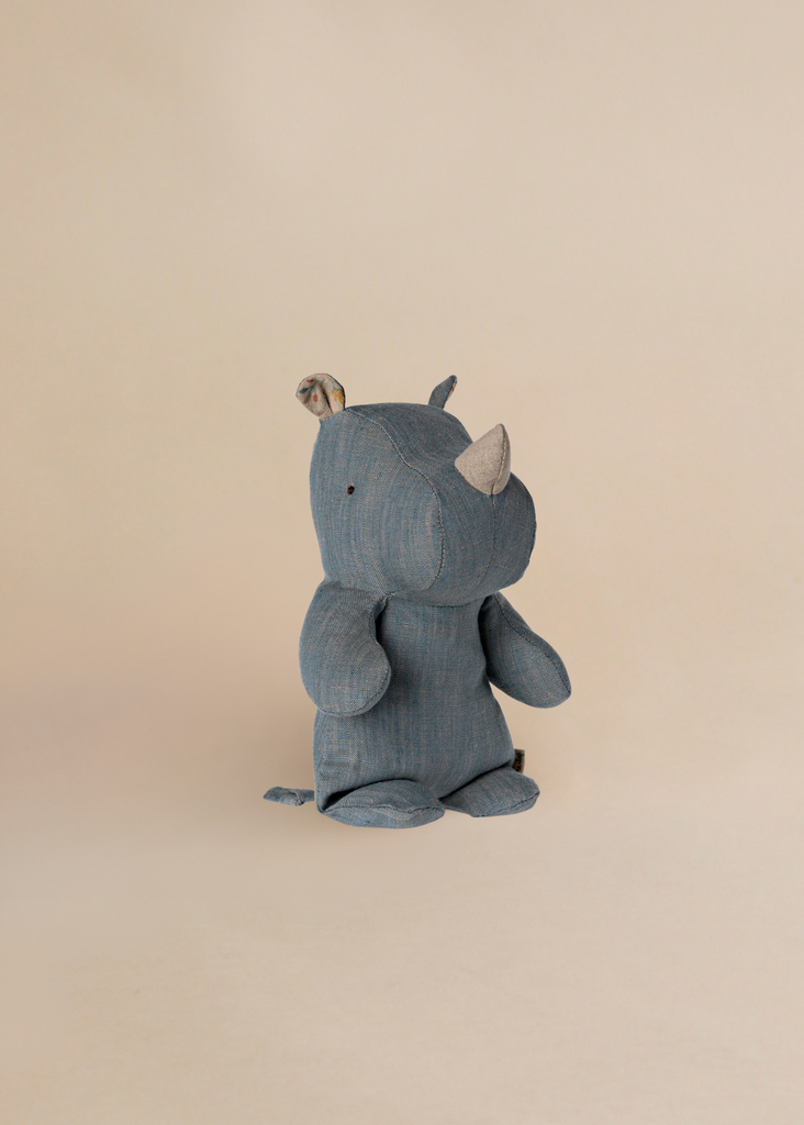 The Maileg Small Rhino - Blue Sand, a soft recycled polyester plush toy from the Safari friends collection, stands upright against a beige background.