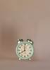 A vintage-style mint green alarm clock with silver bells stands on a plain light brown background, paired perfectly with the charming Maileg Living Room Set, showing the time as 8:00.