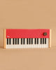 The Complete Set: Loog Piano features wooden sides, a red top panel, black and white keys, a round knob, and the "Loog" logo. Includes piano stand, music stand, sustain pedal, octave shifter & carrying case—ideal for stylish beginners.