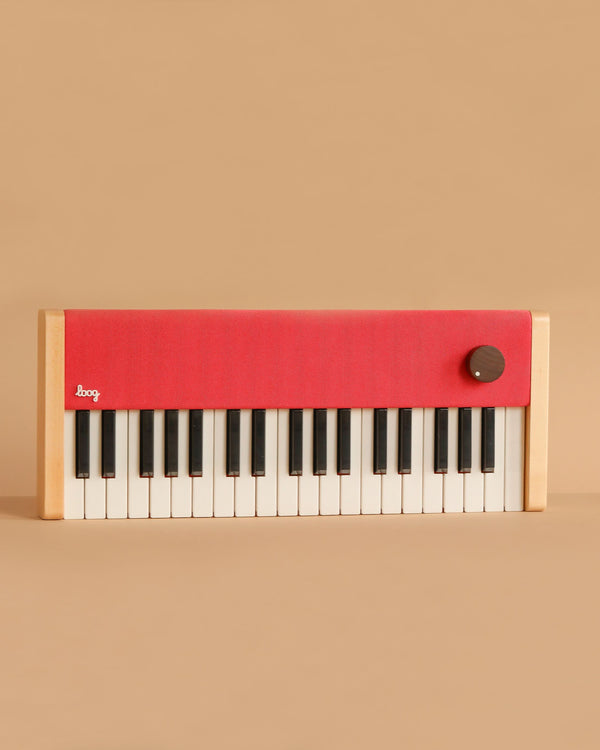 The Loog Piano is a compact, minimalist digital piano featuring wooden sides, black and white velocity-sensitive keys, a bright red top panel, and a single large knob on the right, shown against a plain beige background.