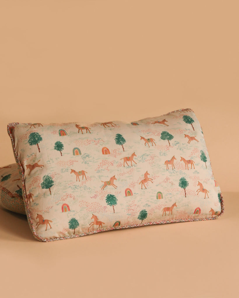 The Maileg Cushion - Unicorn is a rectangular, soft cotton cushion featuring whimsical unicorns, green trees, and colorful rainbows on cream fabric with a solid pale peach back.