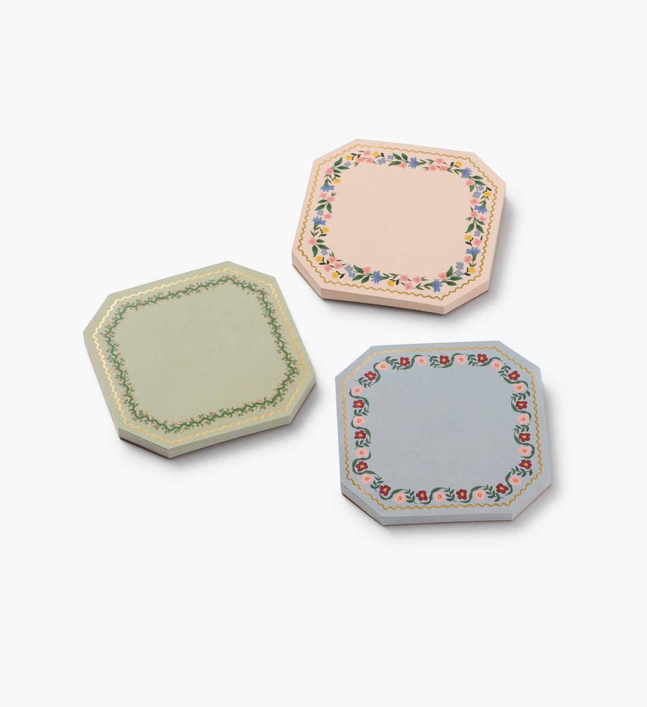 The Gemma Mini Notepad Trio features three decorative octagonal notepads in pastel pink, green, and blue with metallic gold details and floral borders. Each notepad includes convenient tear-off sheets and is displayed on a white background.