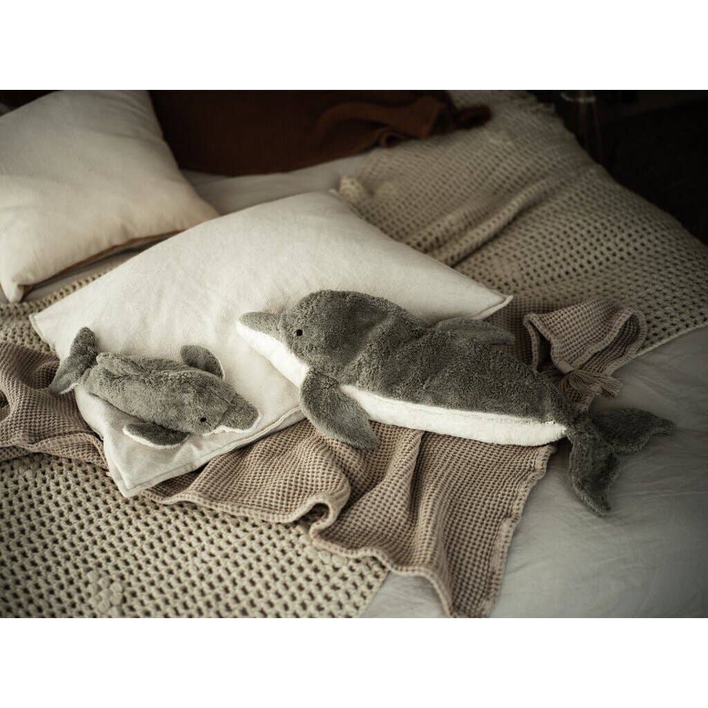 Two Senger Naturwelt Cuddly Animal Dolphin plush toys, one large and one small, sit on cream pillows and a beige textured blanket atop a cozy bed. These soft dolphins are crafted from sustainable materials.
