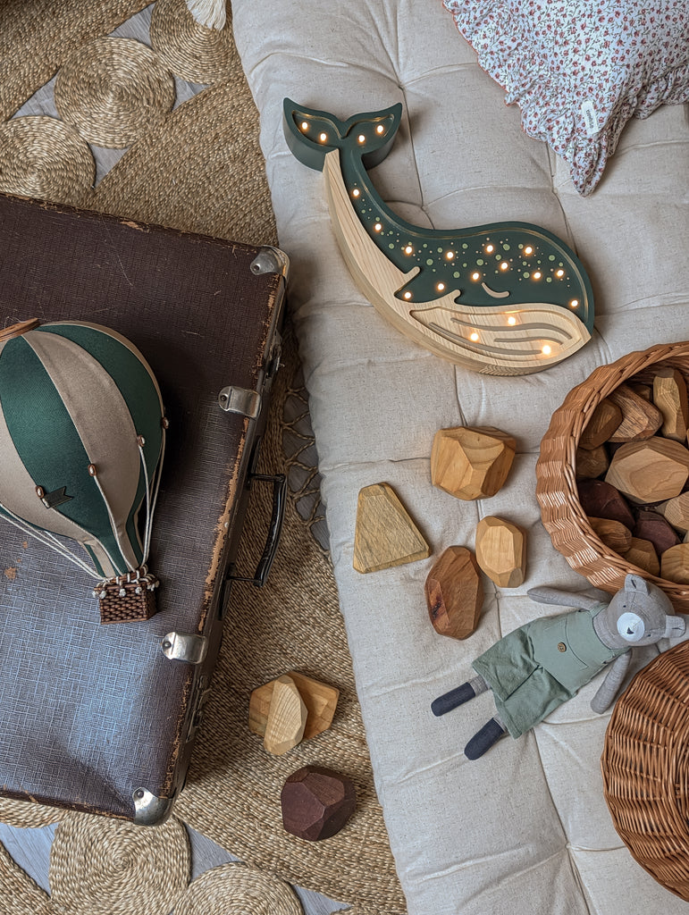 A cozy scene with a vintage suitcase, green whale-shaped night light, Hot Air Balloon - Light Brown / Green decor, wooden blocks, wicker basket, and fabric rabbit doll on a textured rug—perfect for charming children's room decoration.