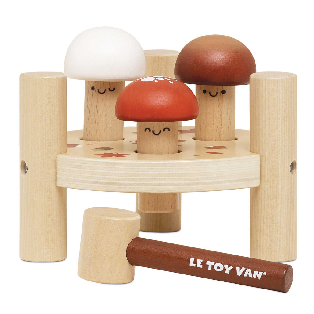 The Woodland Mushroom Hammer Game includes three smiling, mushroom-shaped pegs, a round stand with four posts, and a mallet labeled "LE TOY VAN"—ideal for building fine motor skills.