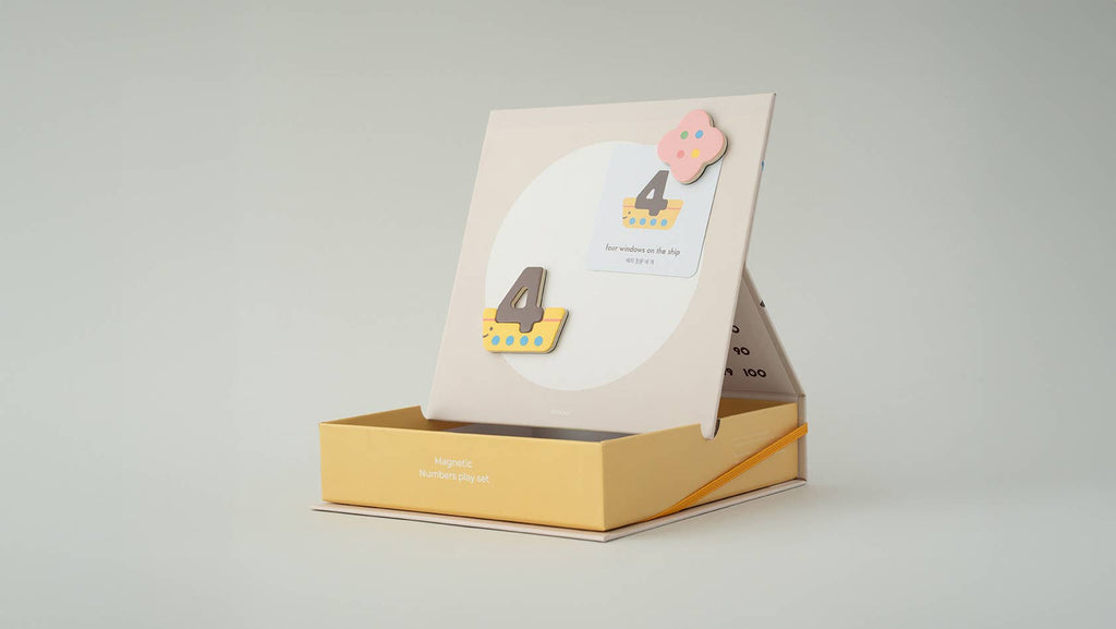 The Magnetic Number Play Set comes in a yellow and white box with a stand, featuring magnetic numbers and colorful shapes. It’s great for kids' numeracy play, wooden toy sets, or magnet puzzle collections. Includes the number 4 and a pink flower magnet.
