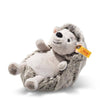 The Steiff Hedgy Hedgehog 6" is a plush toy with soft gray and white fur, a smiling face, small ears, a round nose, and a yellow ear tag. It lies on its back against a plain white background.