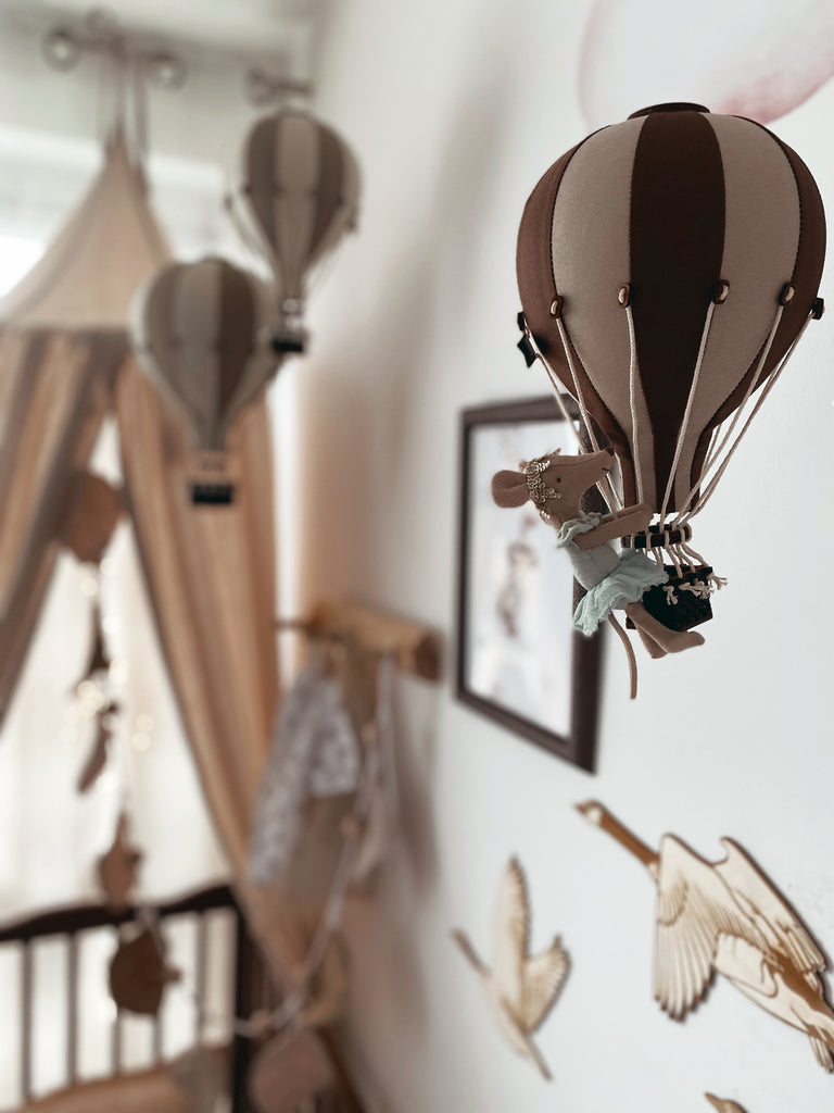 A nursery decorated in soft brown and beige tones features the Light Brown / Dark Brown Hot Air Balloon mobile, wooden bird wall art, and a cozy crib canopy—perfect for children's room decor.