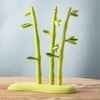 The Bumbu Handmade Wooden Red Panda Family with Bamboo Set features three stylized green bamboo stalks with leaves on a matching base—an ideal Montessori learning toy accent displayed on a wooden surface against a light blue background.